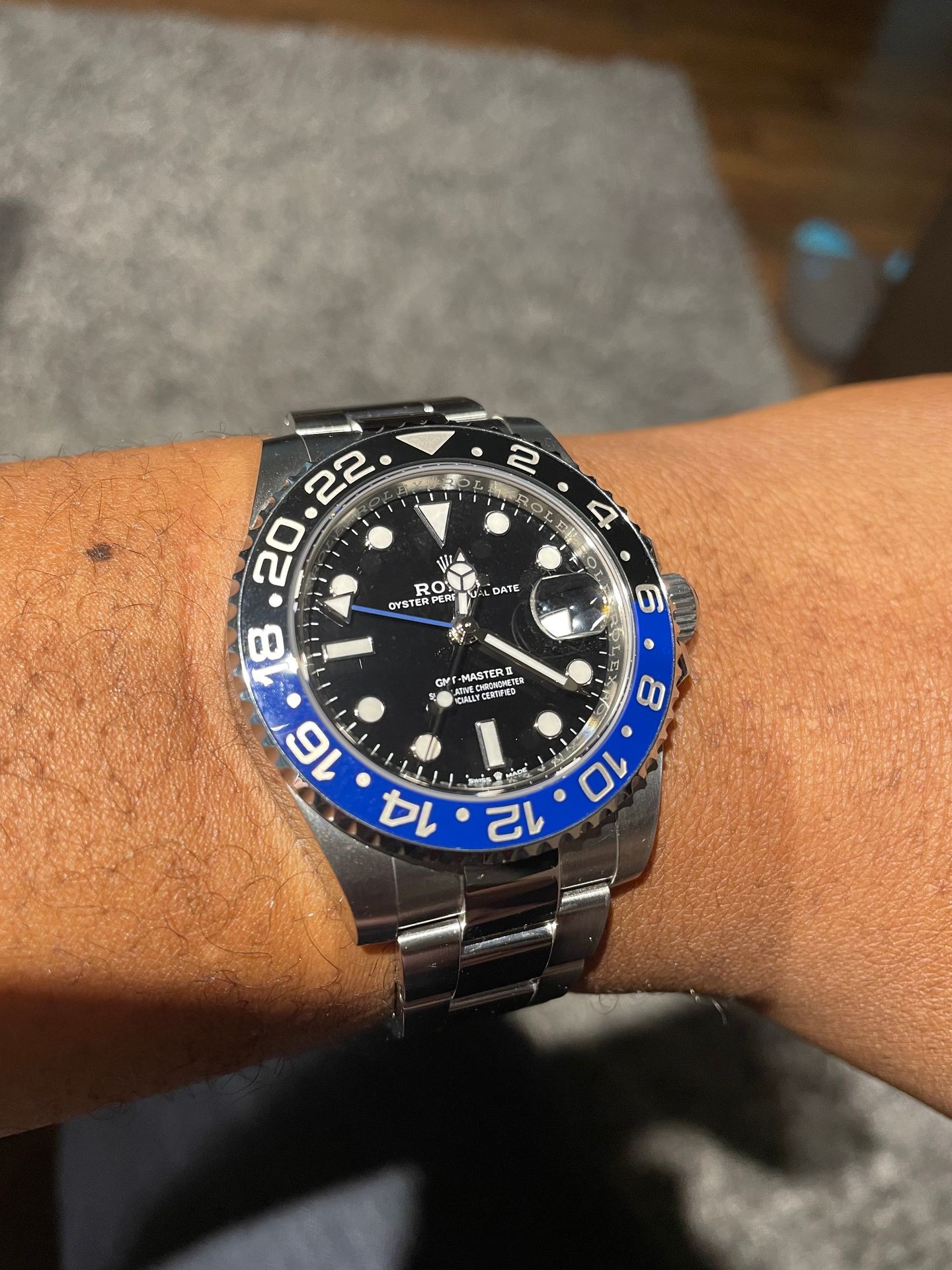 Close-up of a luxury wristwatch with a black and blue bezel on a person's wrist.